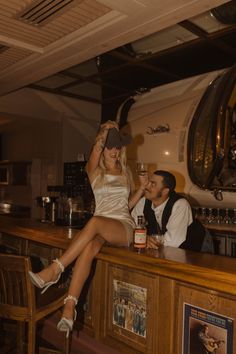 a woman sitting on top of a bar next to a man holding a beer bottle