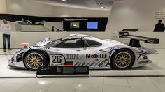 a white sports car on display in a showroom with people looking at the cars