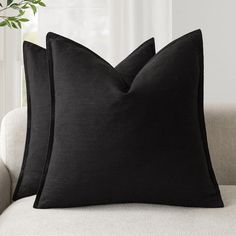 two black pillows sitting on top of a white couch next to a potted plant