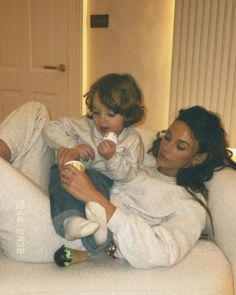 a woman holding a baby while sitting on top of a white couch next to another woman