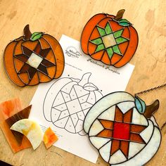 three stained glass pumpkins sitting on top of a table next to a piece of paper