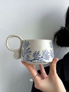 a woman holding up a white and blue coffee cup with leaves painted on the side