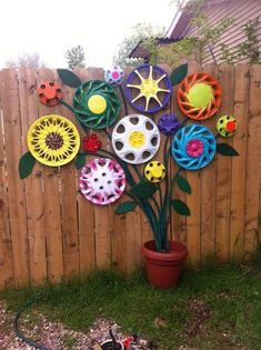 a potted plant sitting next to a wooden fence with paper flowers on it and the words made from hub caps and old garden hoses