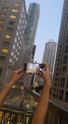 a person holding up a cell phone to take a photo in front of tall buildings