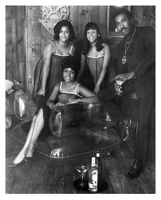 a black and white photo of four people posing for the camera with drinks in front of them