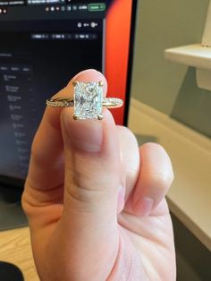 a person holding an engagement ring in front of a laptop