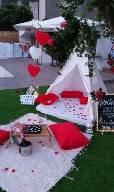 a teepee tent set up in the grass with red pillows and hearts hanging from it