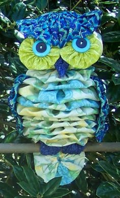 an owl ornament hanging on a tree branch with blue eyes and green leaves