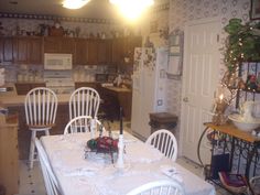 a table with white chairs in a kitchen next to a refrigerator and stove top oven