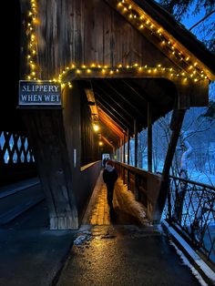 a man is walking down the walkway under a covered bridge with christmas lights on it