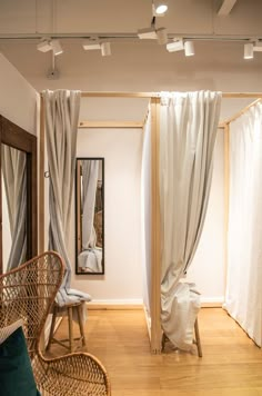 a room with white drapes and wicker furniture on the wooden floor, along with a mirror