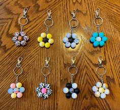 six key chains with different colored beads hanging from them on a wooden surface, one has a flower and the other is a butterfly