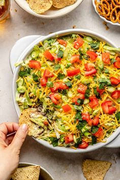 a person dipping tortilla chips into a bowl filled with mexican salad and vegetables