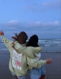 two girls are playing on the beach with their arms around each other as they fly a kite