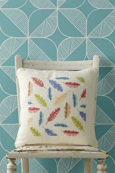 a white chair sitting next to a blue wall with a colorful pillow on top of it