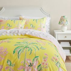 a bed with yellow comforter and pink flowers on it next to a white night stand