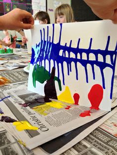 children are painting on paper with blue and yellow paint, while another child is holding up a piece of paper