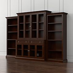 an empty bookcase and cabinet in the corner of a room with hardwood floors, white walls and wood flooring