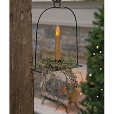 a lit candle is hanging from a metal holder with greenery on the outside and inside