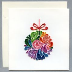 a card with an ornament made out of colored paper on top of a white envelope