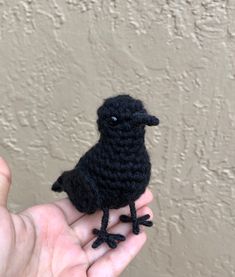 a small black bird sitting on top of someone's hand in front of a wall