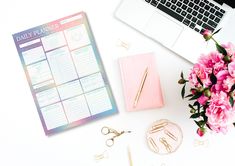 a desk with a laptop, planner and flowers on it