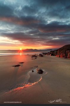 the sun is setting over some rocks on the beach