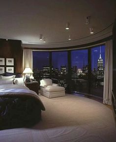 a bedroom with a large window overlooking the city lights and skyscrapers is shown at night