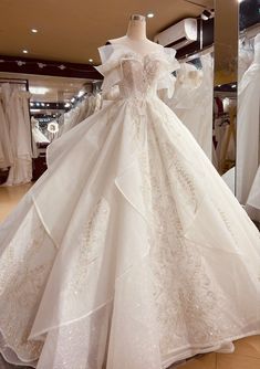 a white wedding dress is on display in a store with mannequins behind it