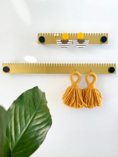 two yellow tassels hanging from hooks on a wall next to a green plant