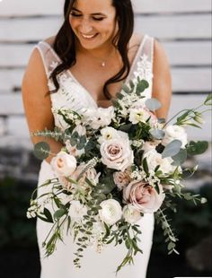 a woman holding a bouquet of flowers and greenery in her hands while smiling at the camera