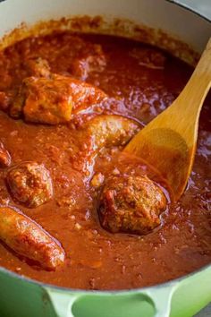 meatballs and tomato sauce in a green pot with a wooden spoon on the side