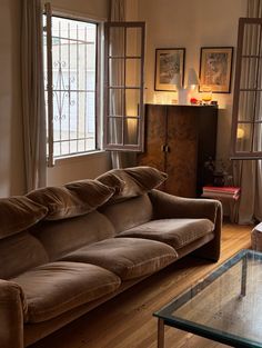 a living room filled with furniture next to a glass top coffee table and two windows