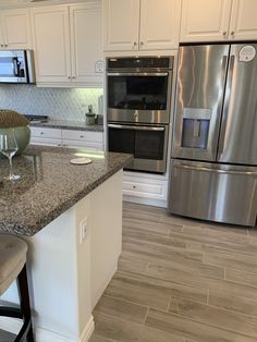 a kitchen with stainless steel appliances and marble counter tops, along with white cabinetry