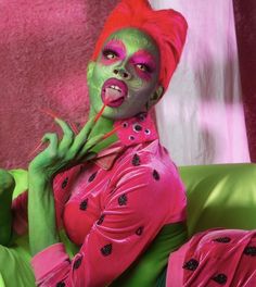 a woman with green and pink makeup is sitting on a couch holding a toothbrush