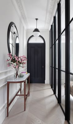 a hallway with black doors and flowers in vases on the side table next to it