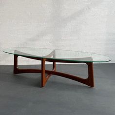 a glass and wood coffee table with curved legs on grey concrete floor next to white brick wall