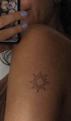 a woman with a small sun tattoo on her arm holding a cell phone and taking a selfie