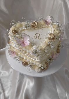 a heart shaped cake with flowers and butterflies on it's side sitting on a white table cloth