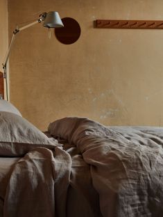 an unmade bed in a bedroom with a lamp on the wall next to it