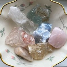 a bowl filled with different colored rocks on top of a white and gold rimmed plate