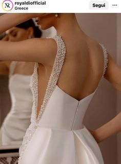 the back of a woman's wedding dress in front of a mirror with her hand on her shoulder