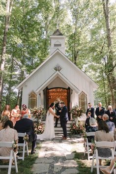 a bride and groom are getting married in front of a small white chapel surrounded by trees