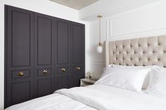 a bed with white sheets and pillows next to a black cabinet in a bedroom that has gold handles on the doors