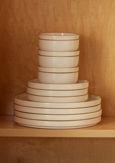 stack of white plates sitting on top of a wooden shelf