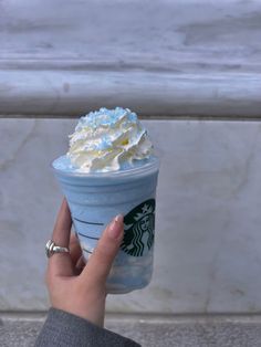 a starbucks cup with whipped cream on top is held up by a woman's hand