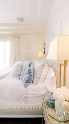 a white bed sitting in a bedroom next to two lamps and a table with flowers on it