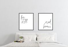 two black and white prints with the words be still and know on them above a bed