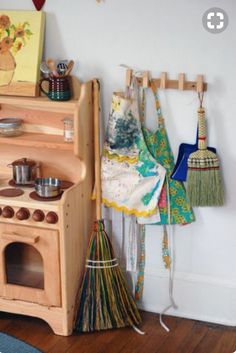 an old fashioned wooden toy stove with brooms and pots on the rack next to it