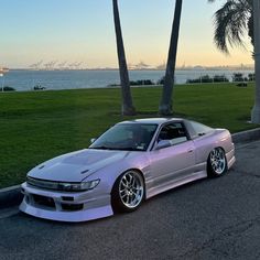 a silver car parked on the side of a road next to palm trees and water